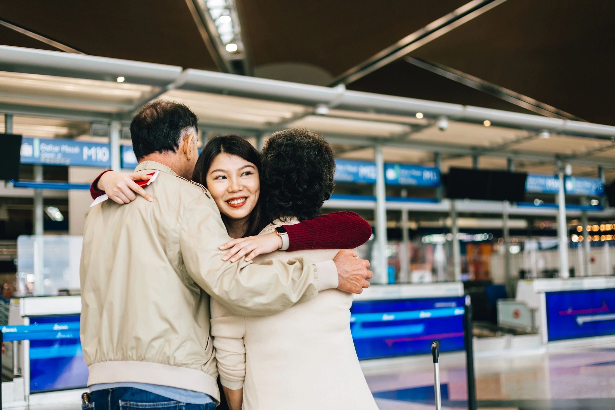 Family reunion at the airport — parents welcoming their child with a warm hug after travel.