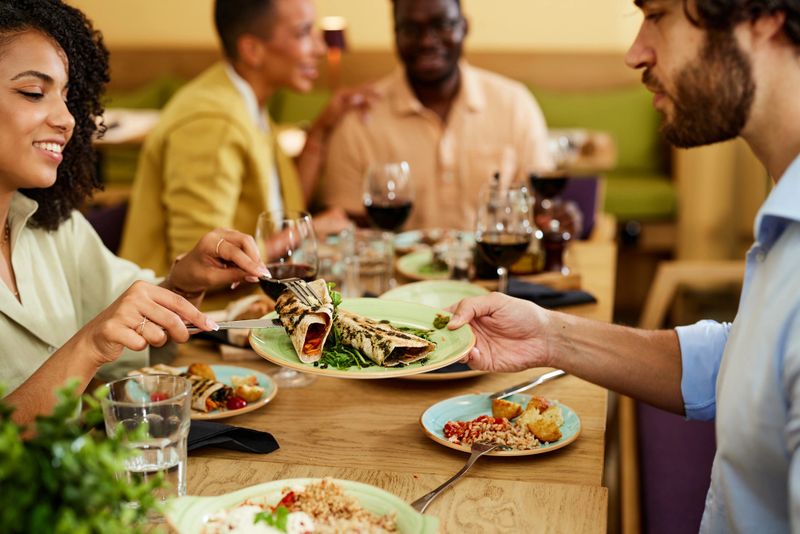 A happy woman is taking food from a plate that the man is holding. Dinner party in a restaurant concept.