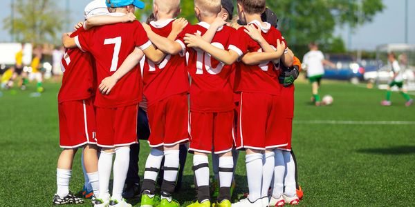 Kids in red soccer uniforms huddle together on the field.