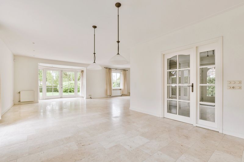 Interior of light spacious living room tiled floor with big window and curtains and wide glass door leading to backyard on sunny day