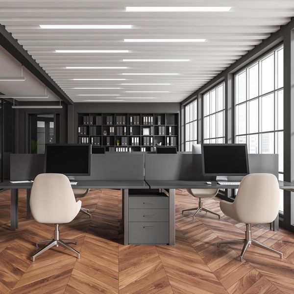 Modern office workspace with computers, beige chairs, and large windows.