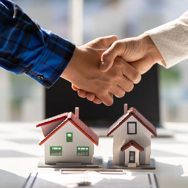 Partners shaking hands over the 3D image of two houses. 