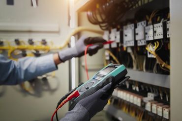 Technician using a multimeter to check electrical circuits in a control panel.