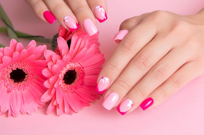 Beautiful female hands with romantic manicure nails, pink gel polish, gerbera flowers design