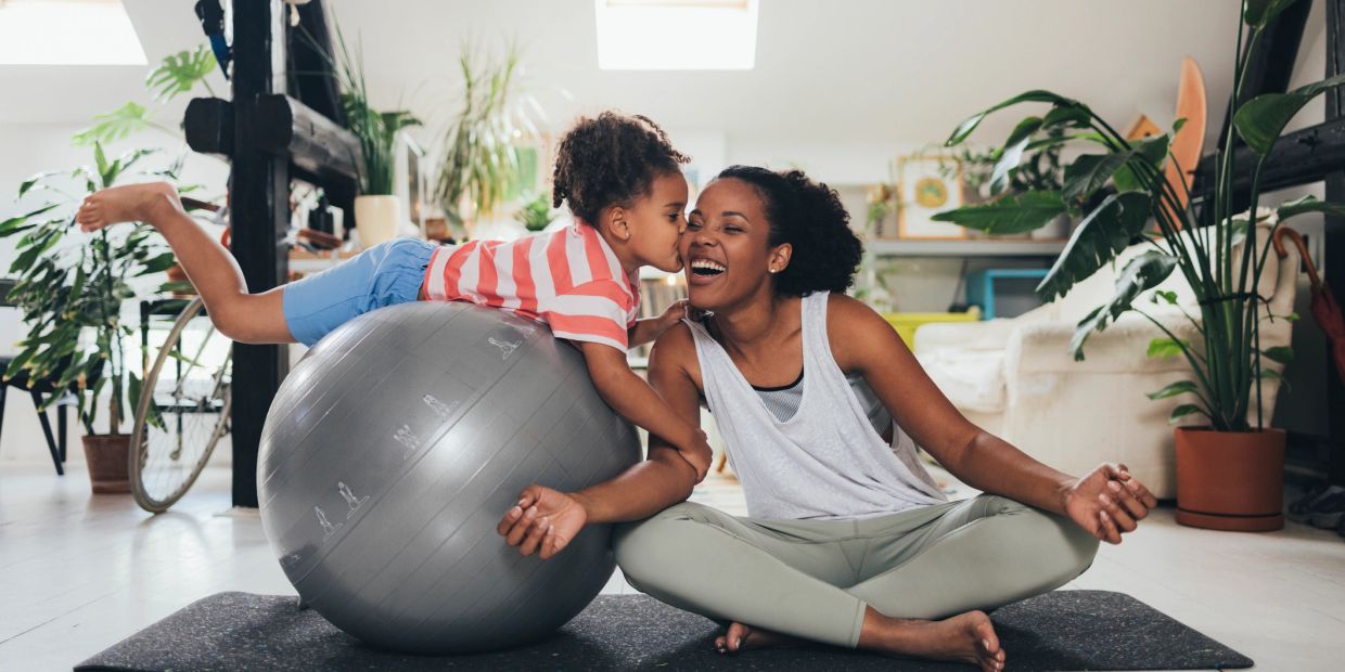 Child kisses mother while balancing on exercise ball.