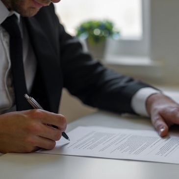Businessman signing documents at a desk with a laptop and calculator.