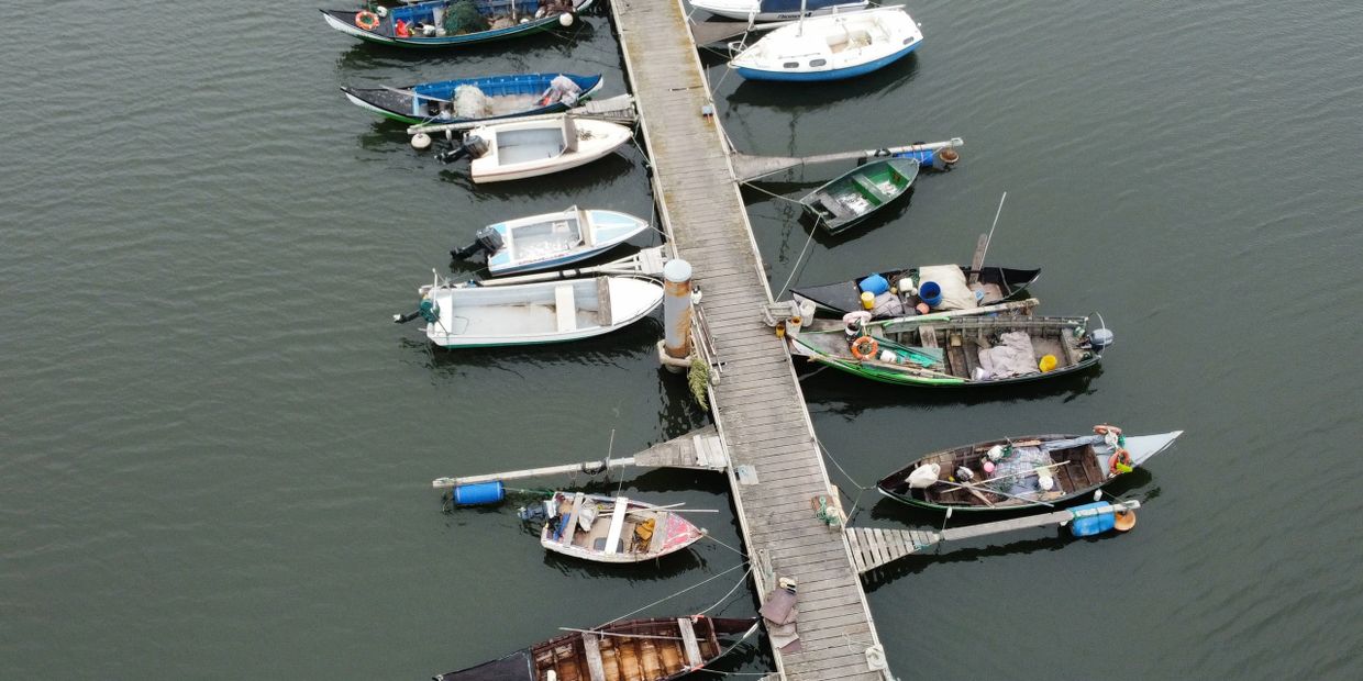 Aerial view of small boats docked along a wooden pier in calm water.
