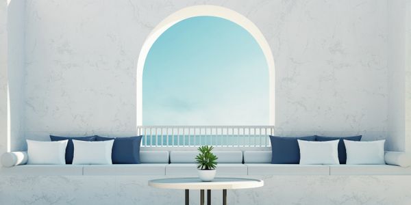 Minimalist white seating area with blue and white pillows by an arched window.