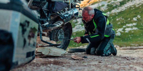 Man fixing motorcycle tire on rocky ground.