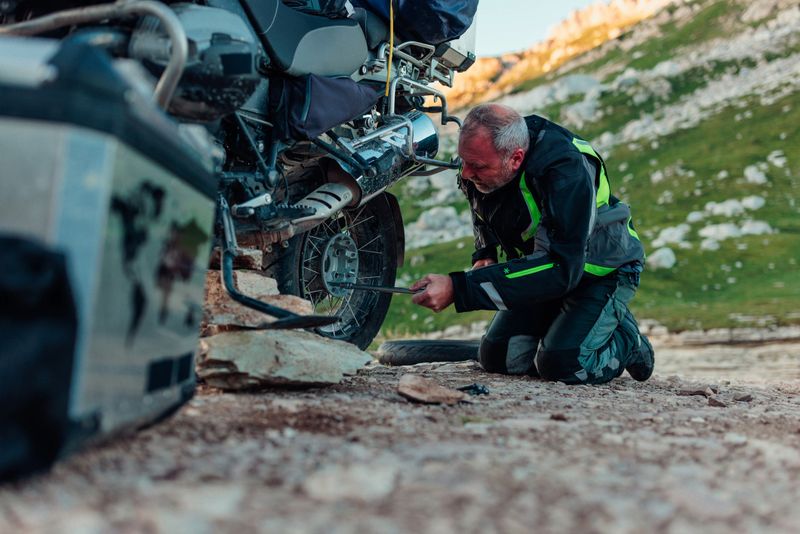 Senior motorcyclist changing tire on his motorbike after he had an accident on the off-road trip