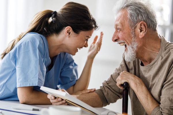 A nurse and elderly man share a joyful moment laughing together.