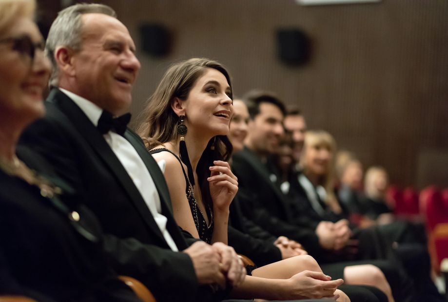 Audience dressed formally, attentively watching an event with smiles and interest.