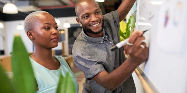 Two colleagues collaborating and writing on a whiteboard in a modern office.