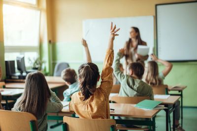 Students raising hands in classroom.