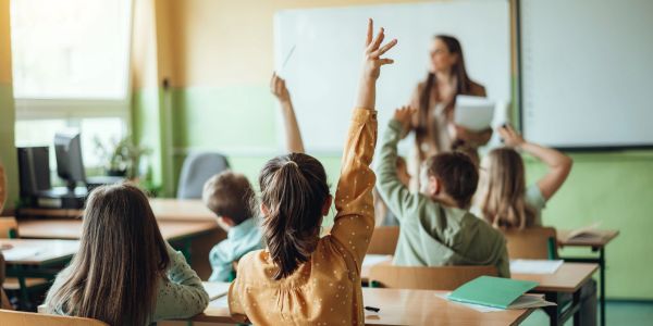 Students raising hands in classroom.
