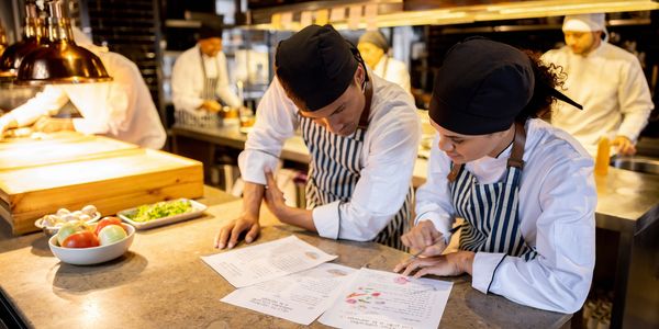 Chefs in a busy kitchen reviewing menus and planning dishes together.