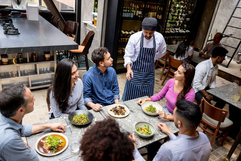 Chef talking to a group of Latin American friends eating together at a restaurant - food and drink service concepts