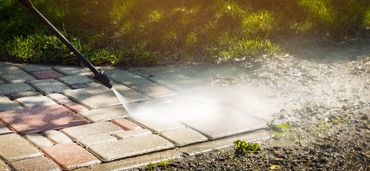 Pressure washing a paved walkway to clean dirt and grime.