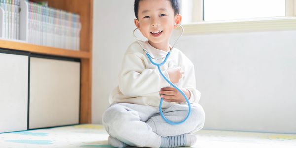 A young boy happily plays doctor with a stethoscope indoors.