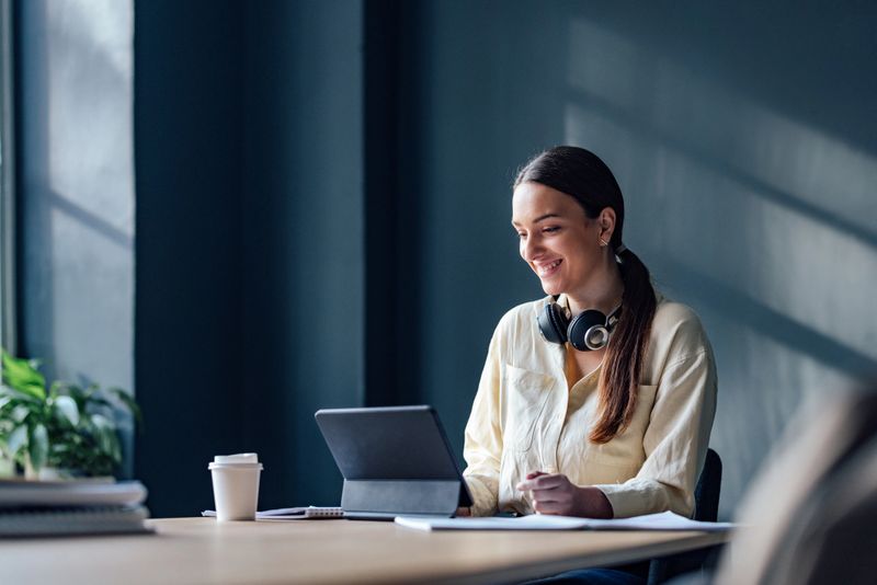Smiling woman sitting at desk and reading online lesson on her tablet in the library.
