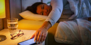 Person reaching to turn off alarm on phone in bed.