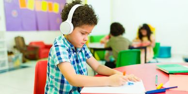 Young boy wearing headphones drawing in a classroom.