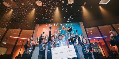 A team celebrating victory with medals and a large check on stage.