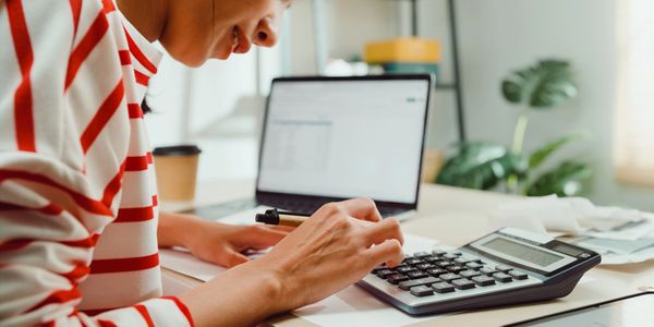 Person using calculator with laptop in the background.
