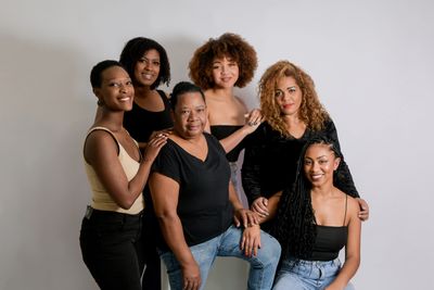 A diverse group of six women posing together against a neutral background.
