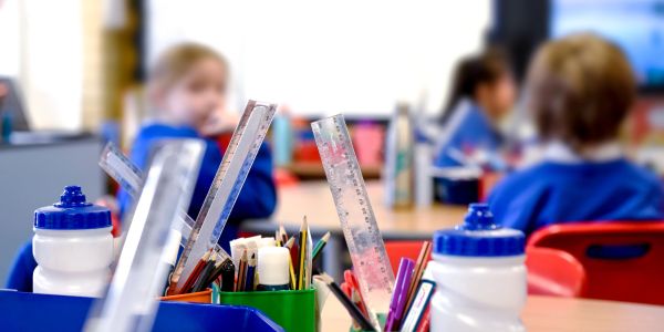 Classroom supplies and blurred students in background.