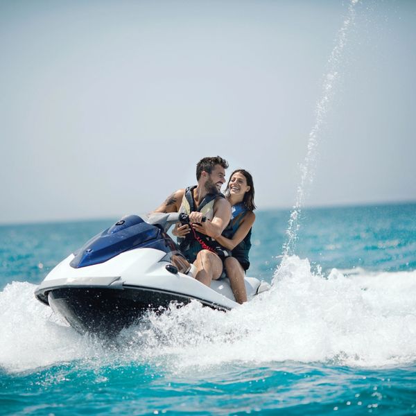 A happy couple riding a jet ski on clear blue water.