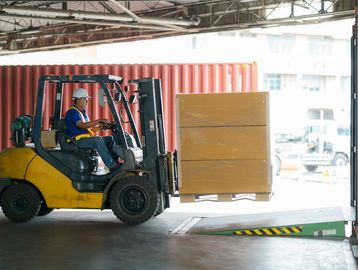 A worker operates a forklift to load a large pallet inside a warehouse.