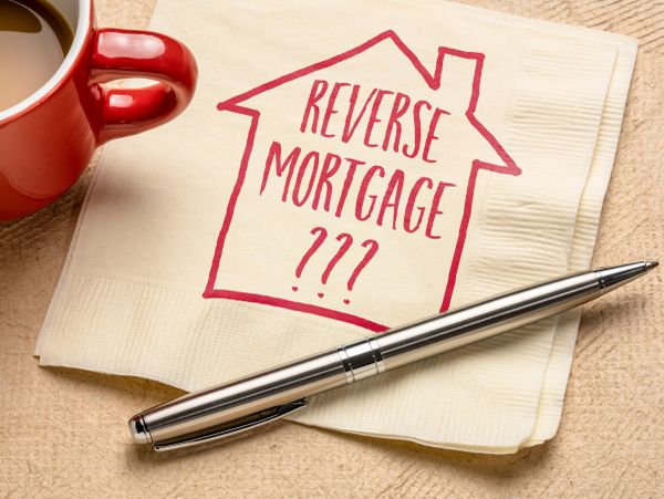 Napkin with 'Reverse Mortgage???' and a pen beside a red coffee cup.