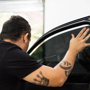 Man inspecting car window with tattoos on arm.