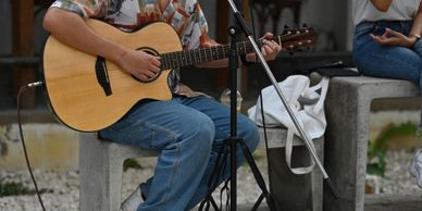 Person playing an acoustic guitar while seated outdoors.