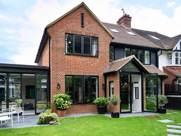 Modern brick house with large windows and a lush green lawn.