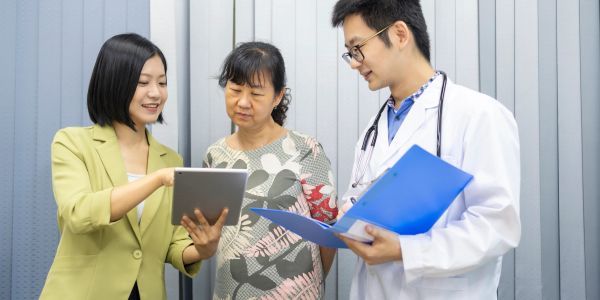 Woman showing tablet to doctor and senior woman in clinic.