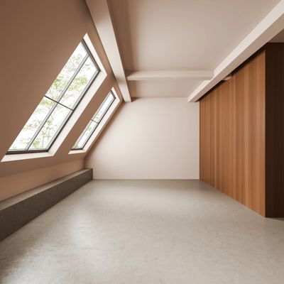 Empty attic room with large slanted windows and wooden panel wall.