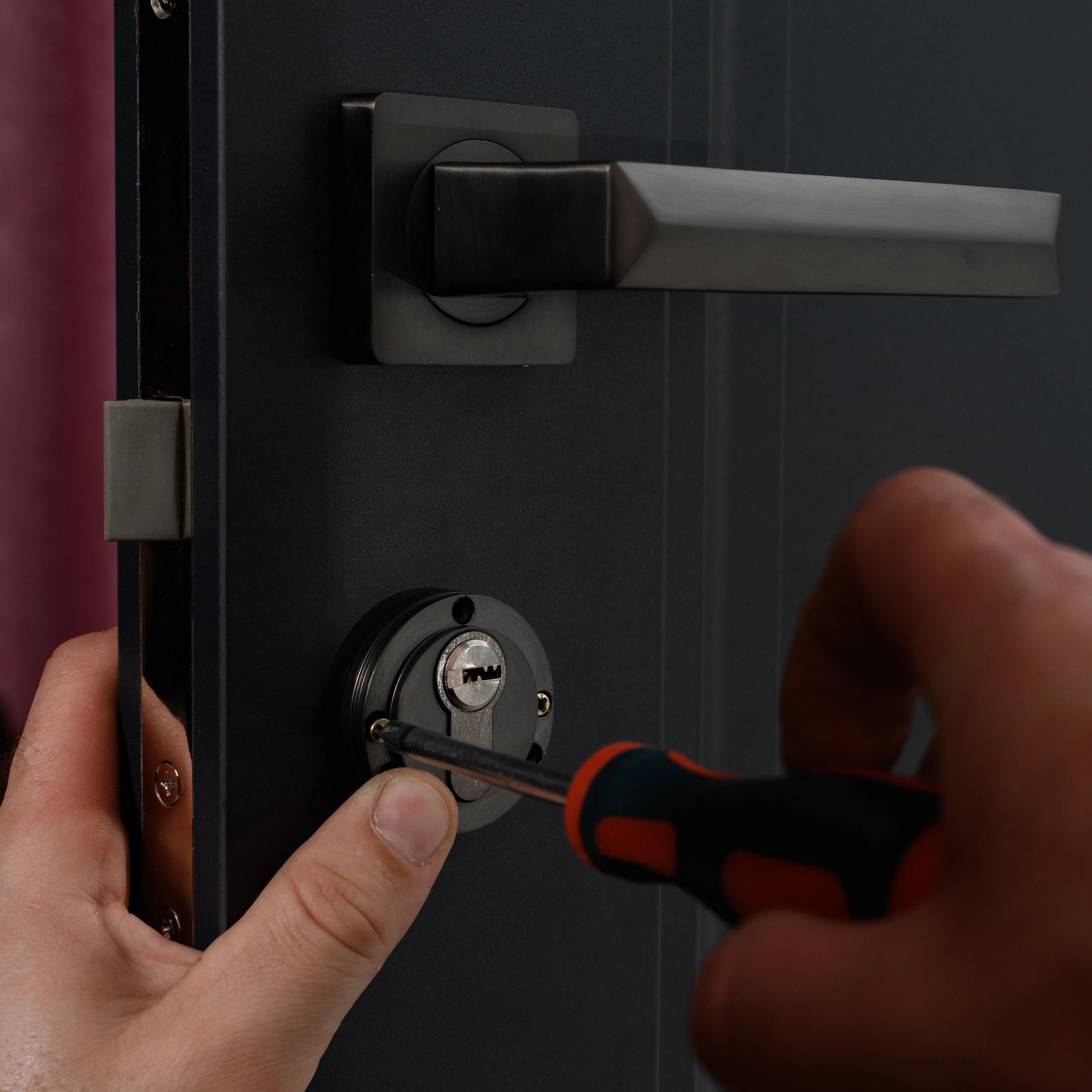 Close-up of a person installing a lock on a dark door with a screwdriver.