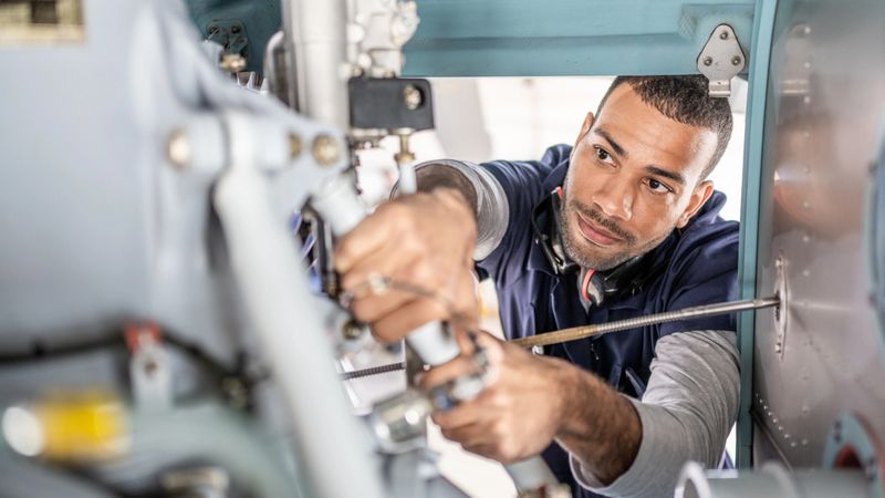 Aviation mechanic repairing jet, inside of engine view. Handsome African American engineer examining aircraft, close up