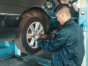 Mechanic using power tool to fix a car tire in a garage.