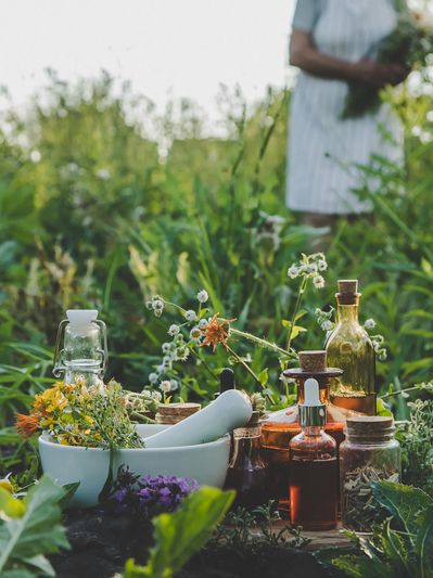 Herbal bottles and mortar in a lush green garden with a person in the background.