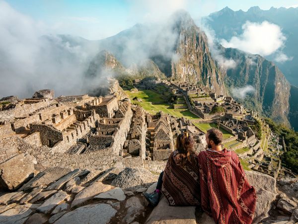 Couple enjoying the view of Machu Picchu ruins surrounded by mountains and clouds.