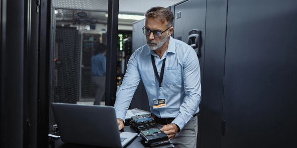 IT technician working with hard drives and laptop in a server room.