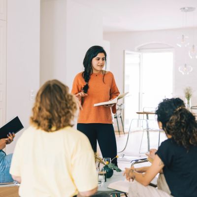 Woman leading a discussion with a group in a bright room.