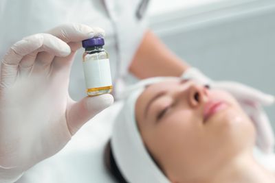 Gloved hand holding a small vial near a woman's face in a clinical setting.
