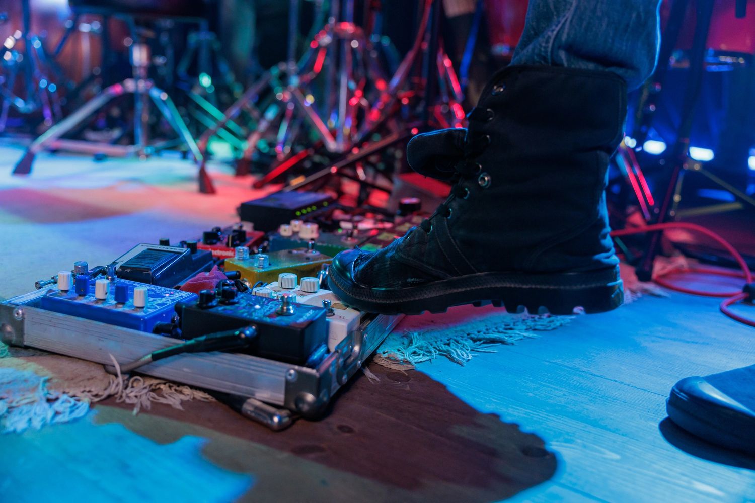 Close-up of a boot stepping on guitar effect pedals during a live performance.