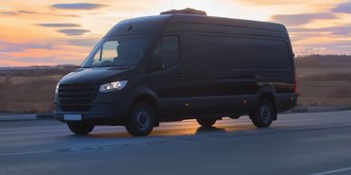 Black delivery van driving on road at sunset.