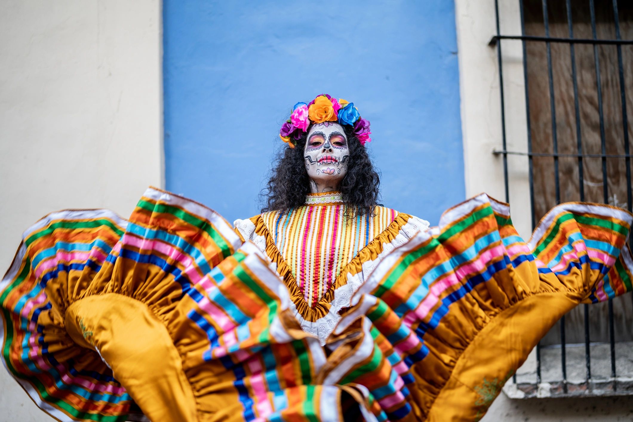 Person in colorful traditional dress and Day of the Dead face paint with flower crown.
