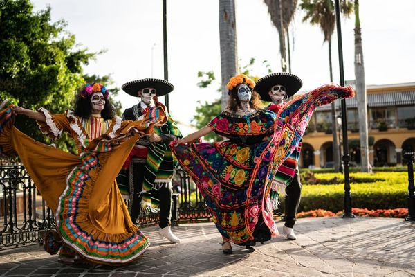 Dancers in traditional Mexican attire with Day of the Dead face paint perform outdoors.